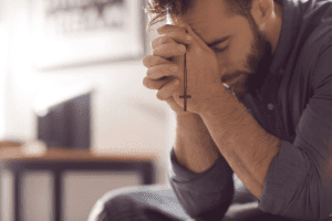 man seated on couch clutching crucifix and fighting drug addiction with religion