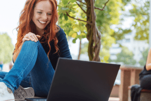 young woman sitting on park bench smiling while working on a laptop and learning your career after alcohol rehab can be rewarding