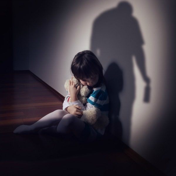 Child cowering in shadow of alcoholic man