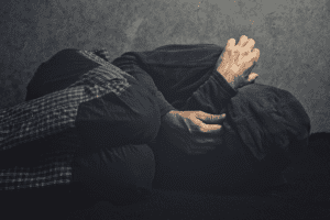 man in dark clothing and hooded jacket in fetal position on the ground experiencing the risks of crystal meth abuse and addiction firsthand