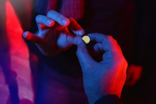 Hand passing a pill to another hand in a nightclub