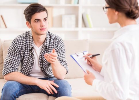 Young man sitting on couch talking to therapist with clipboard