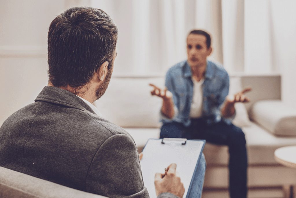 A patient sits on a couch while a therapist takes notes and explains to the patient about what is dialectical behavior therapy