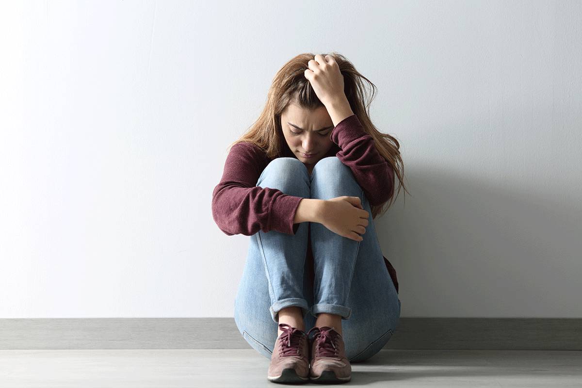 woman sits on the floor holding her hair appearing distraught while experiencing withdrawal symptoms