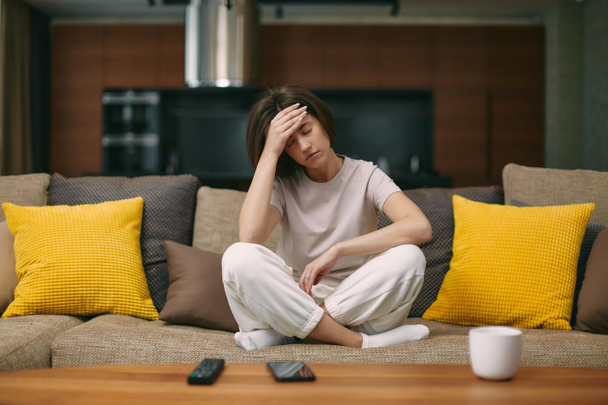woman sits on her couch holding hand to her head thinking about the signs of opioid addiction