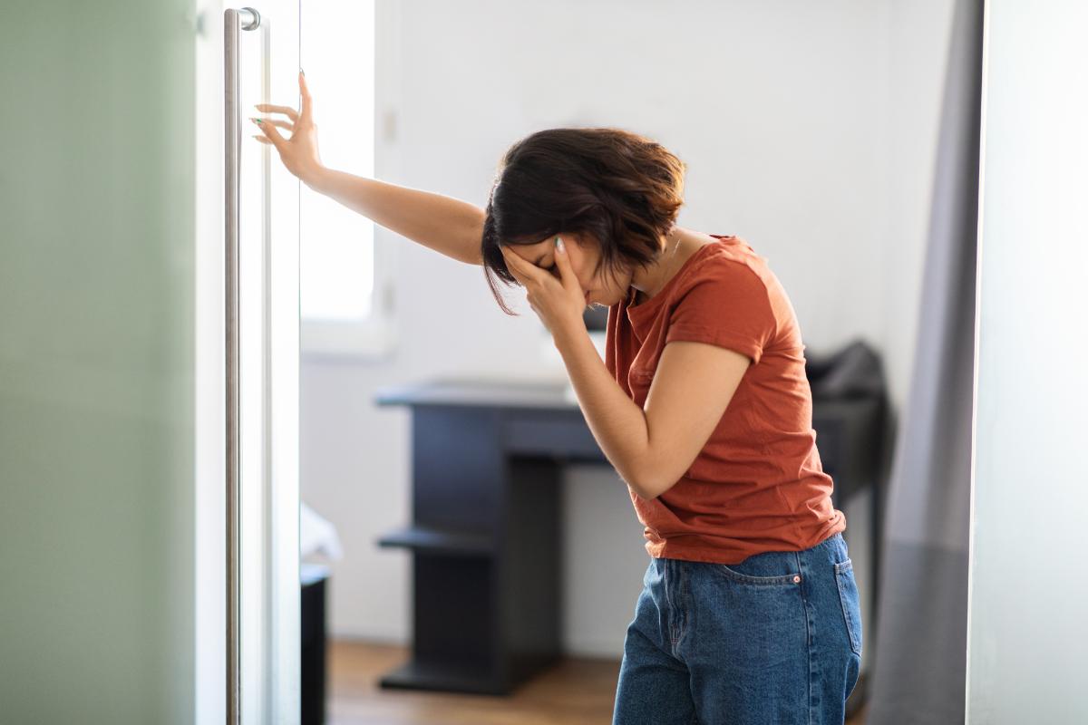 woman stands in doorway and holds her hand in her face struggling with toxic shame and addiction