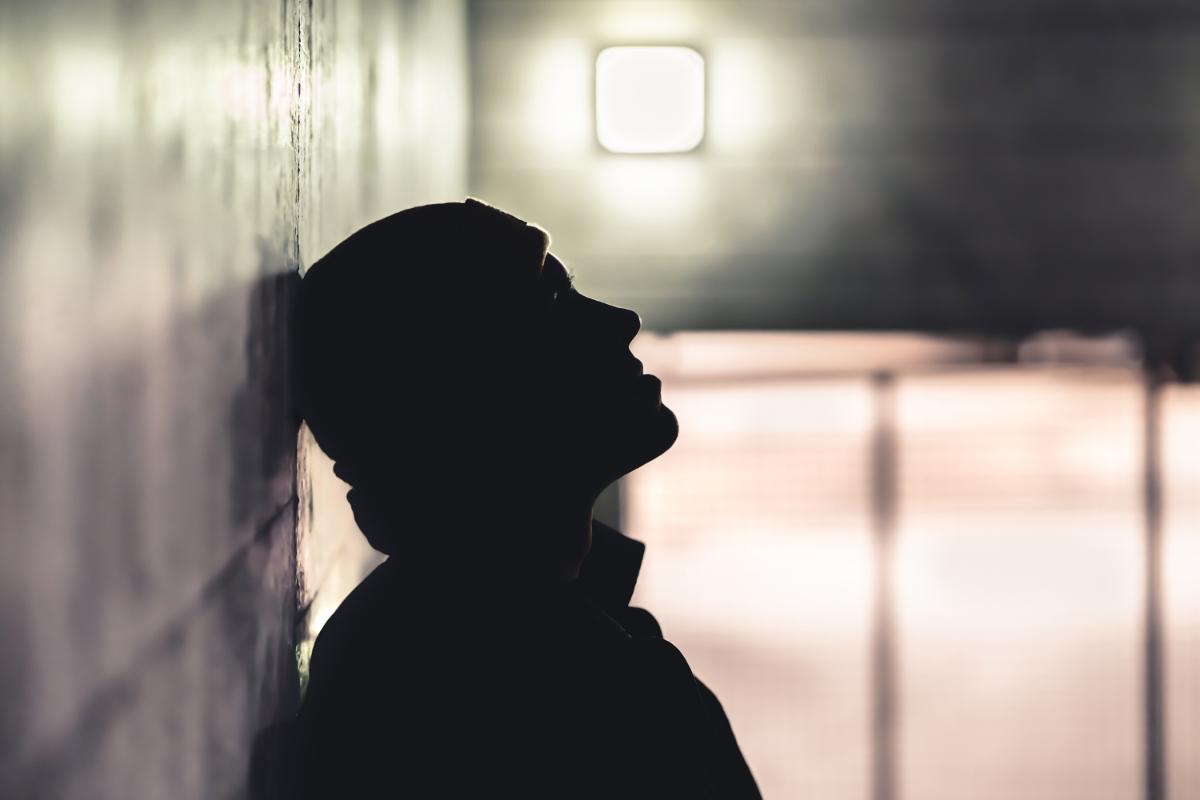Person stands in the dark and leans their head against the wall struggling with toxic shame