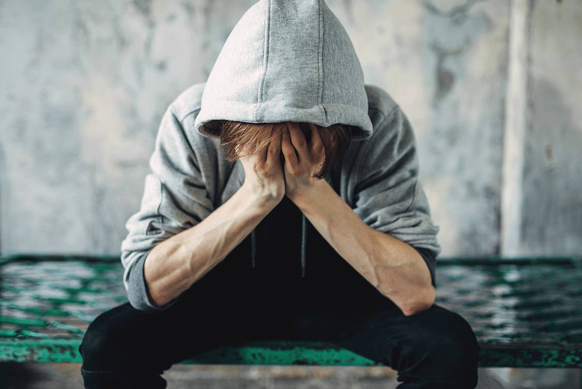 man wearing hoodie sits on a bench and leans his head into his hands struggling with librium withdrawal symptoms
