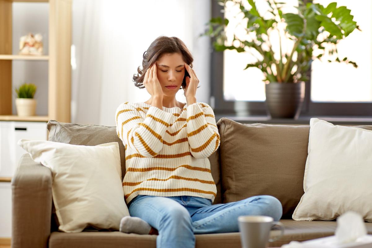 woman sits on the couch hold her hands to her temples wondering if she is experiencing the signs of dxm addiction