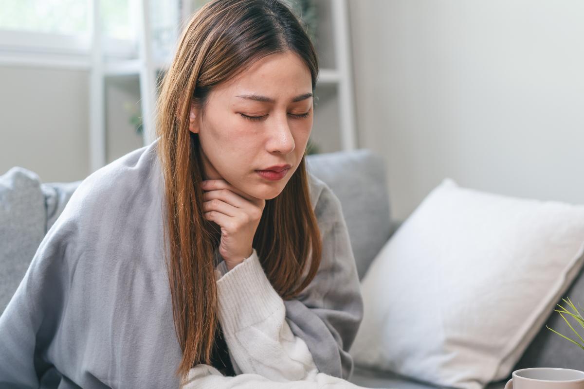 Woman sits on a couch with a blanket over her struggling in pain and wondering what is dxm