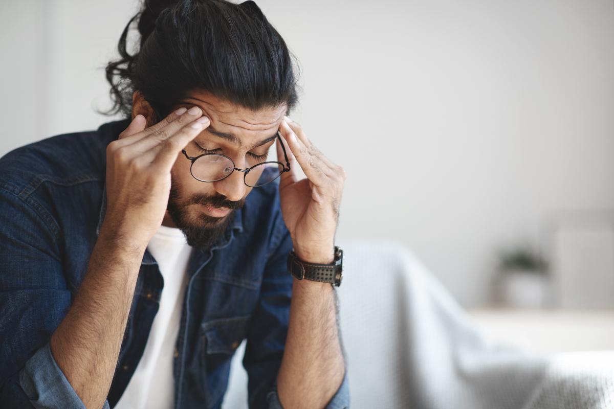 man with glasses leans over and holds his hands to his temples struggling with the aftermath of xanax blackout symptoms