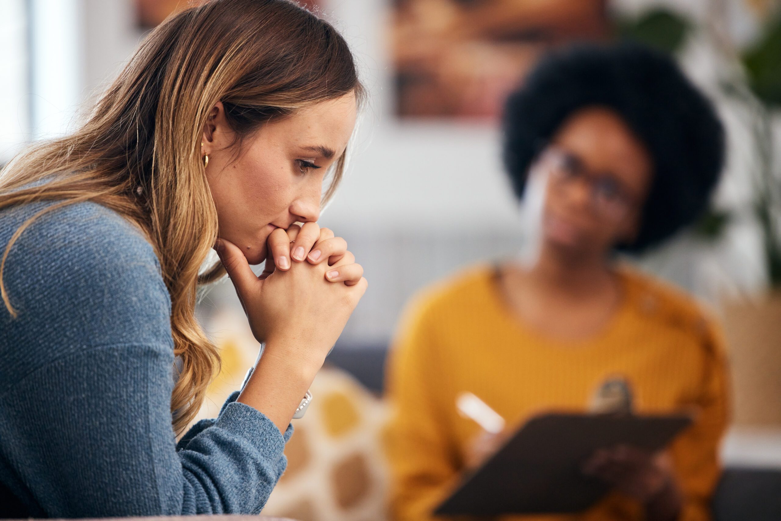 distraught woman rests her face on her hands while looking down and thinking is alcoholism hereditary as her therapist sits and takes notes on her clipboard