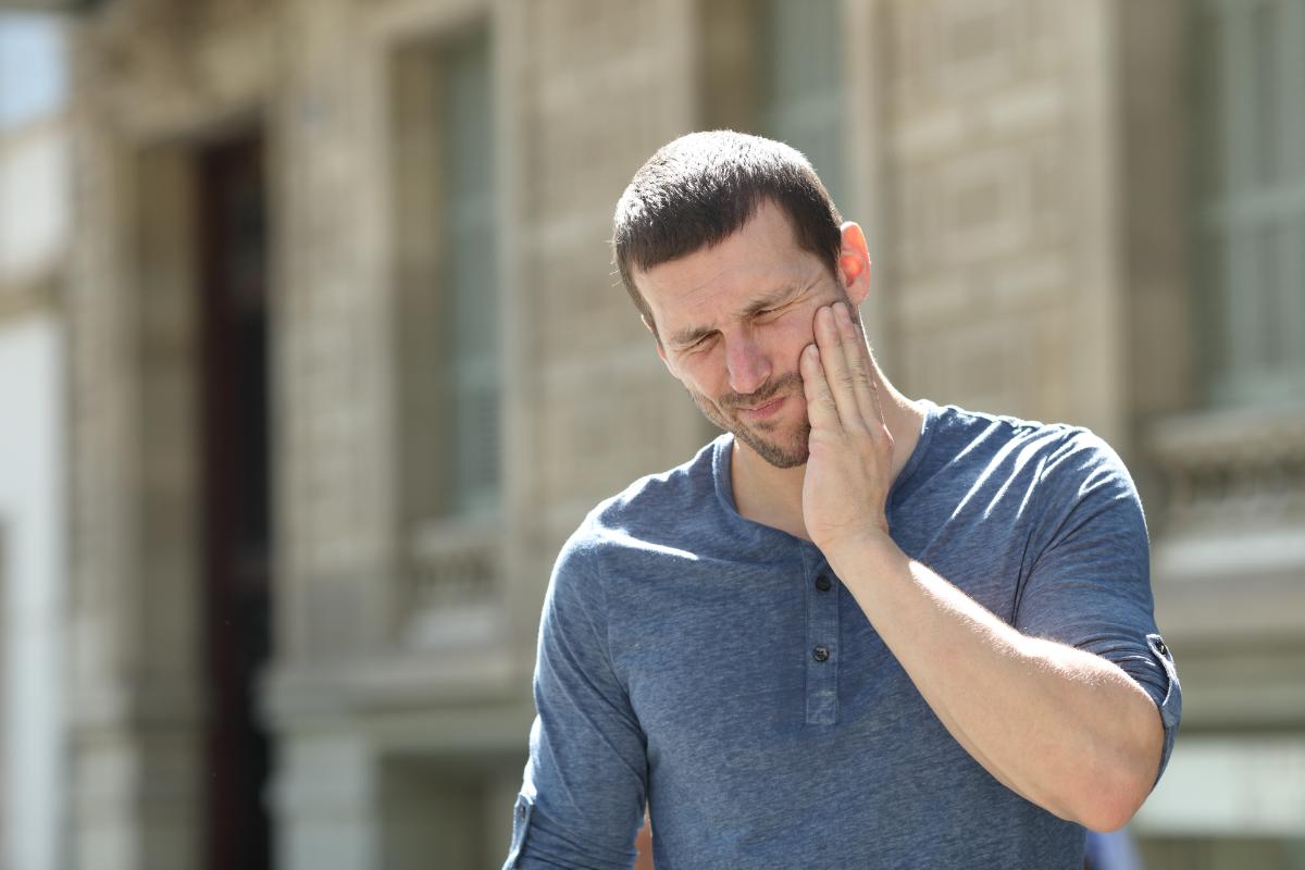 man walks outside and holds his hand to his jaw in pain asking himself what is coke jaw