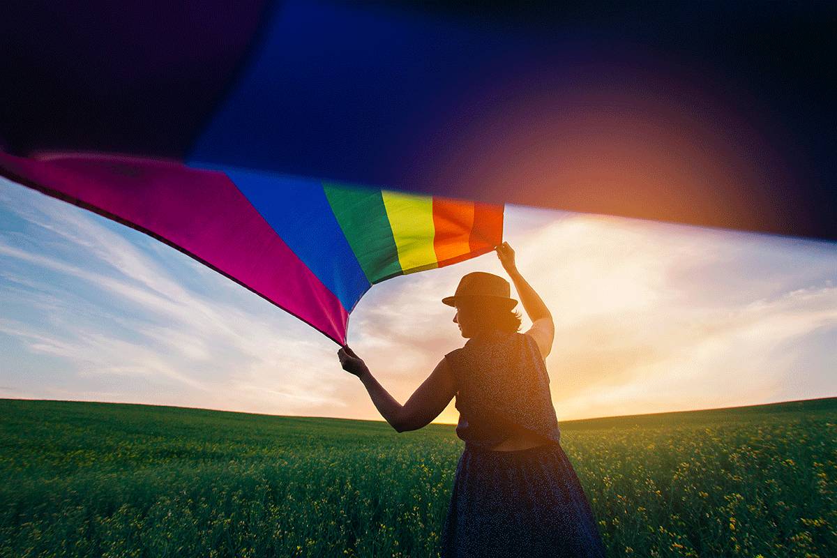 a person in LGBTQ dual diagnosis treatment holds a rainbow flag outside as the sun sets